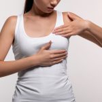 A woman in a white tank top holding her breast, possibly preparing for a breast pump fitting. This image highlights the importance of determining the correct flange size for comfortable and effective breast pumping.