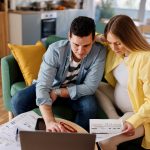 A pregnant woman and her partner reviewing documents and using a laptop, likely researching the cost to get a breast pump. The image reflects planning and budgeting for baby-related expenses.