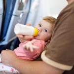 A baby being bottle-fed while sitting on a caregiver's lap during a flight, illustrating the convenience of traveling while breast pumping. This image highlights how pumped milk can make feeding easier when on the go.