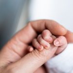 Close-up of a newborn's tiny hand gently holding an adult's finger, symbolizing love and support. This image reflects tips for preemie moms on providing comfort, care, and nurturing to their little ones.