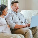 Pregnant woman and her husband on a couch looking at their laptop looking for a Free Breast Pump Through Insurance