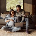 Happy pregnant woman in the living room with her husband looking at the computer showing him the Pumps for Mom ordering process.