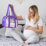 A pregnant woman collects baby things in a purple tote as she begins her hospital bag packing