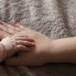 Baby's hand resting on woman's hand -- which is resting on her swollen stomach, a result of postpartum edema