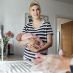 Image of a mother in striped dress holding an infant while using the willow breast pump