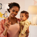 woman wearing Portable Breast Pumps holding infant looking at a mobile